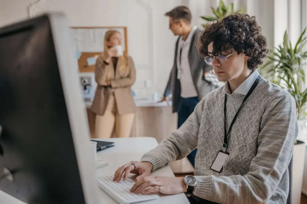 Man working on computer while co-workers chat in background.