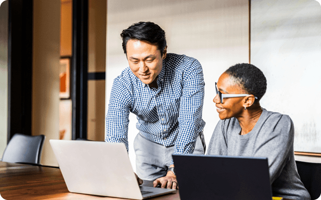 A man showing a smiling women something on his laptop.