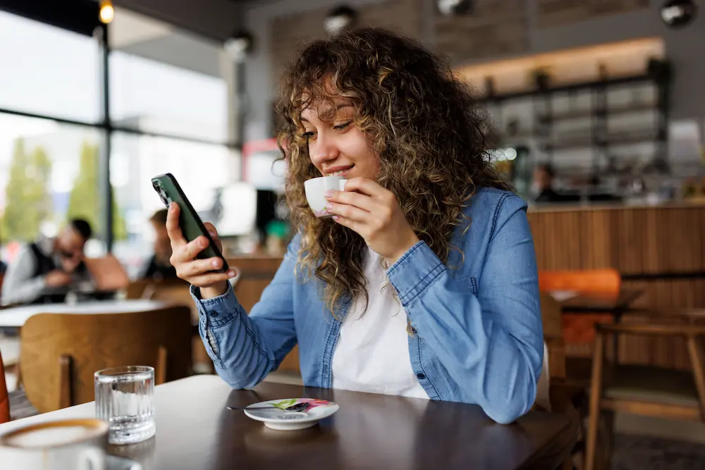 Woman enjoying her expresso while reading email on her phone.