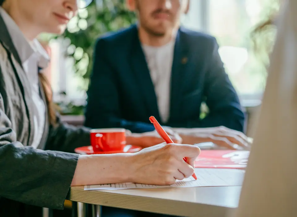 Person in meeting writing with red pen.