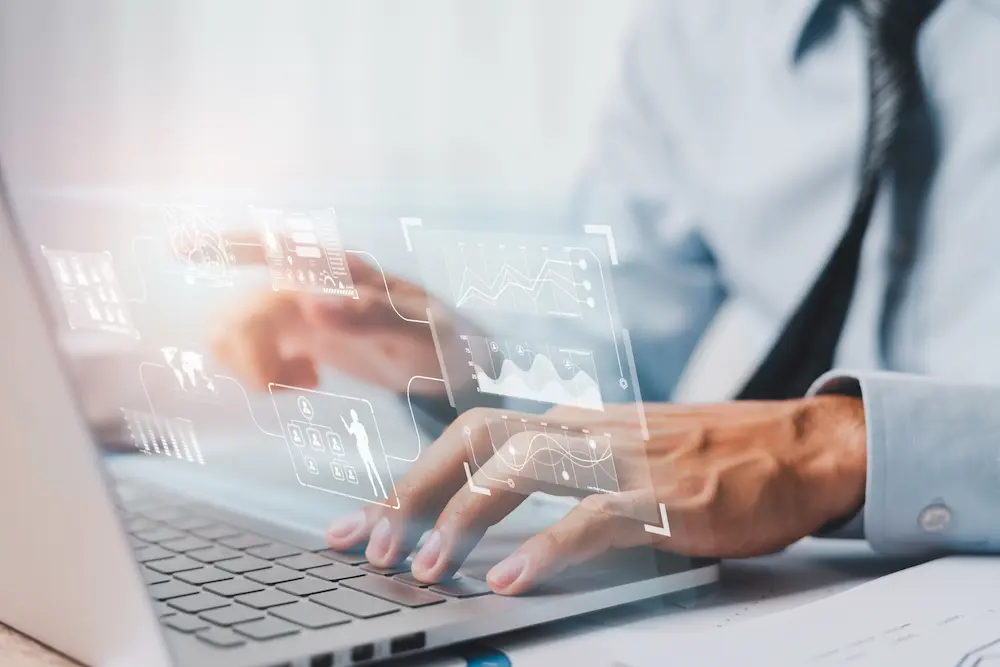 Photo illustration of hands typing on laptop keyboard below digital cloud.