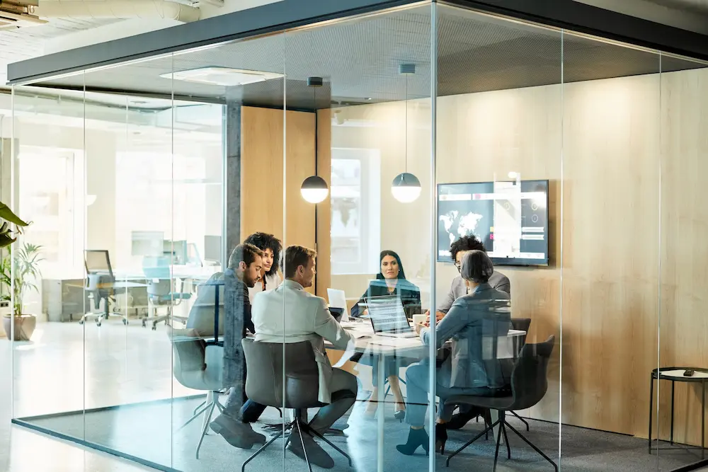 Group of coworkers meeting in conference room discussing business communications compliance and archiving.