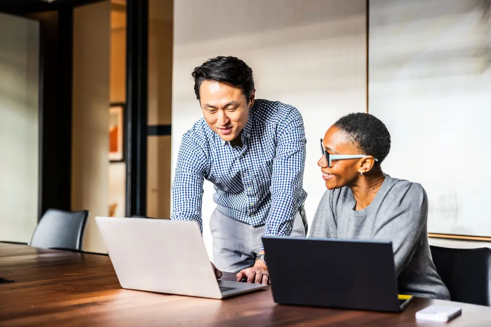 Office workers viewing laptop screen together.