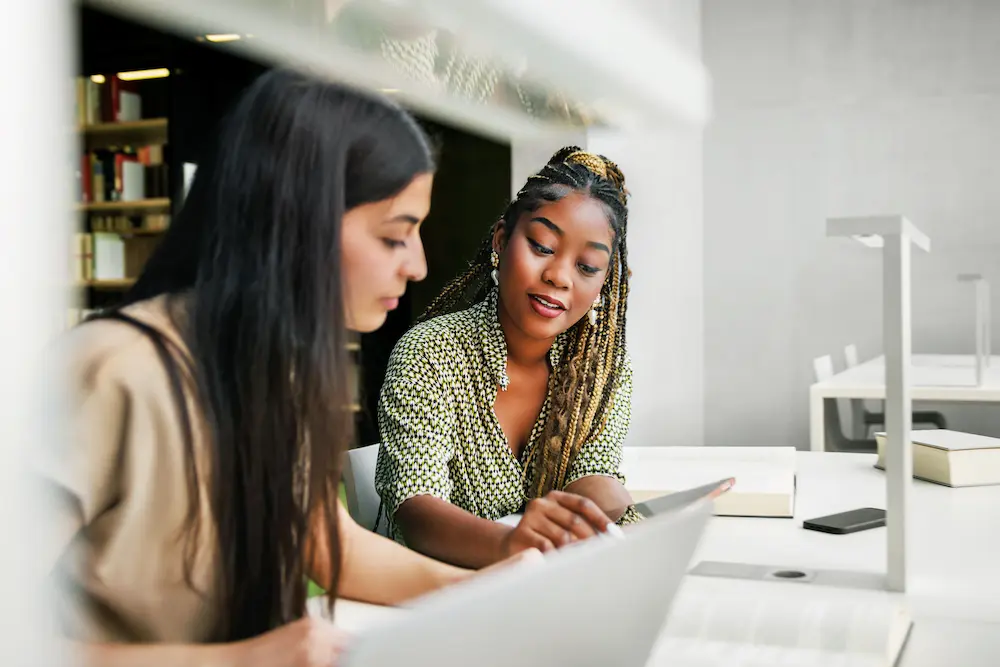 2 women viewing laptop and mobile devices side by side.