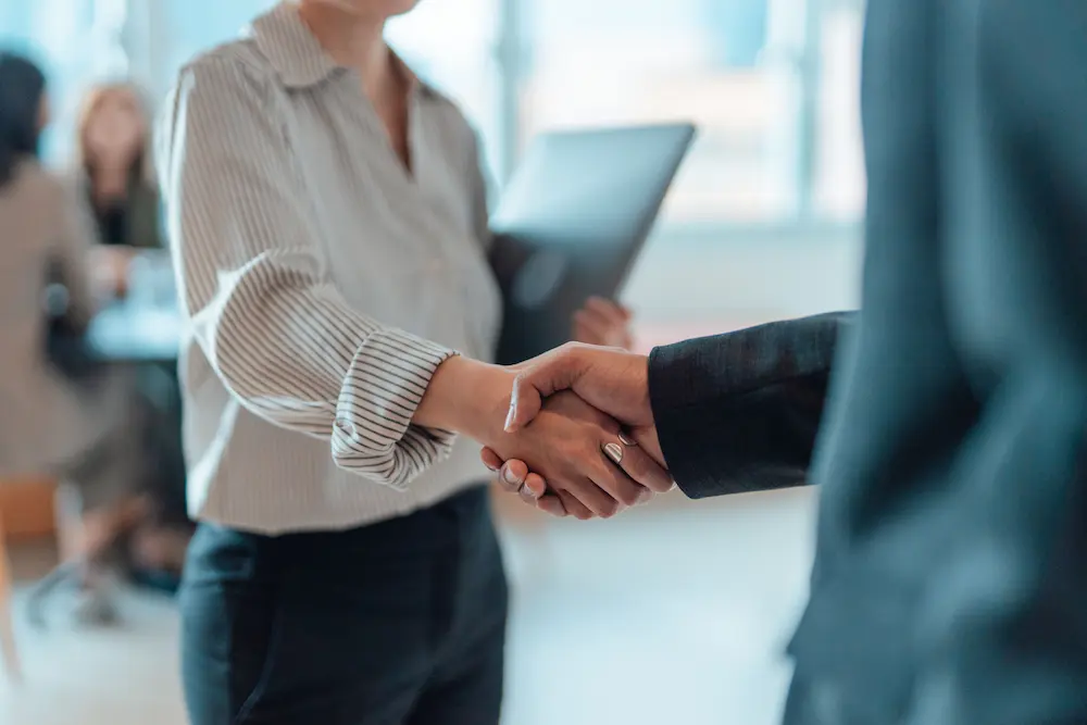 Photo of 2 men shaking hands, pictured from neck to waist.