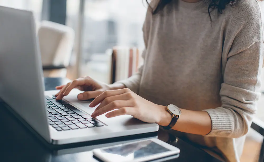 Photo of woman, pictured from neck down, typing on laptop PC.