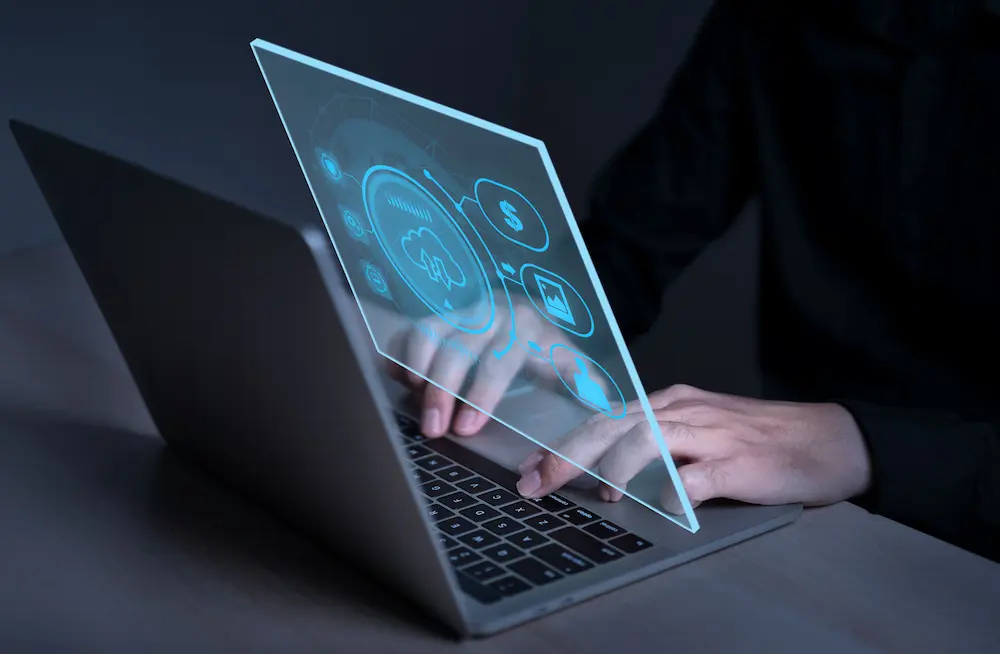 Photo illustration of hands typing on laptop PC surrounded by digital cloud.